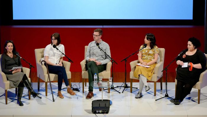 Five panellists sitting on a stage. From left to right: an Indigenous woman, a white woman with a walking stick, a white man, an Asian woman, and an Indigenous woman.